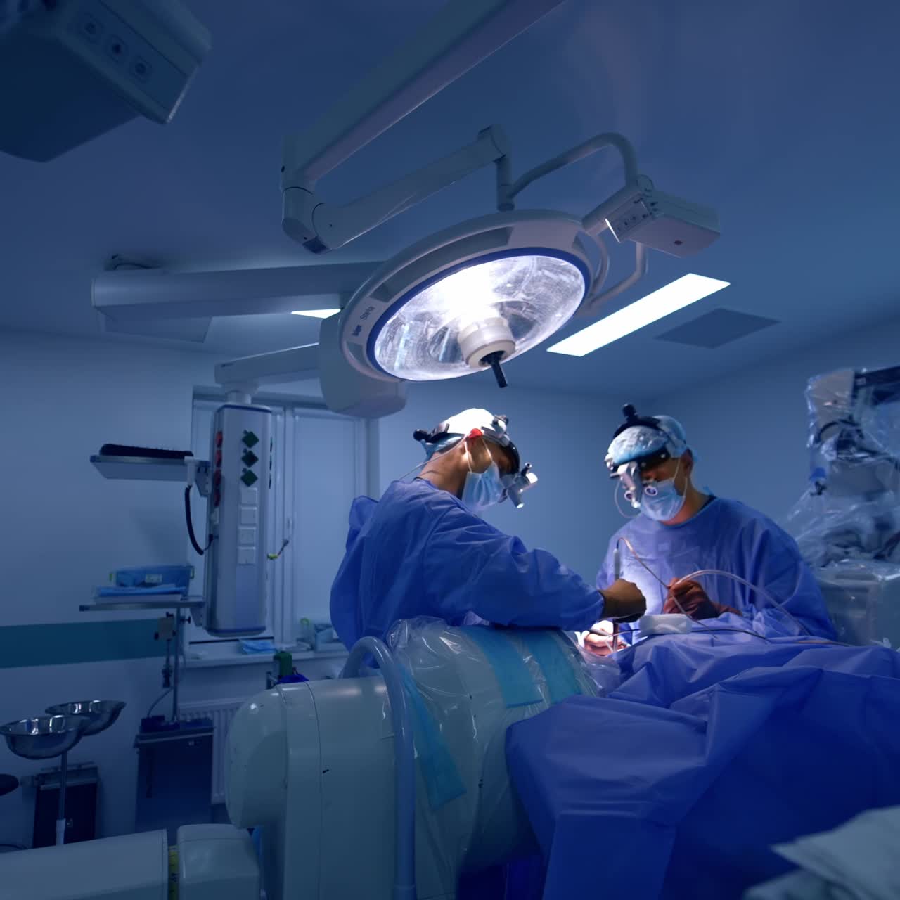 Rummeligt, nyt og moderne operationsstue med neurokirurgi i gang. Et par kirurger udfører operationen under den klare lampe.