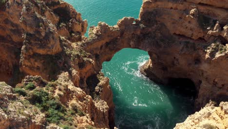 Eroded-Stone-Arch-'Catedral'-above-Algarve's-Coastline-sea-in-Lagos-Portugal---Aerial-crane-down-descending-shot