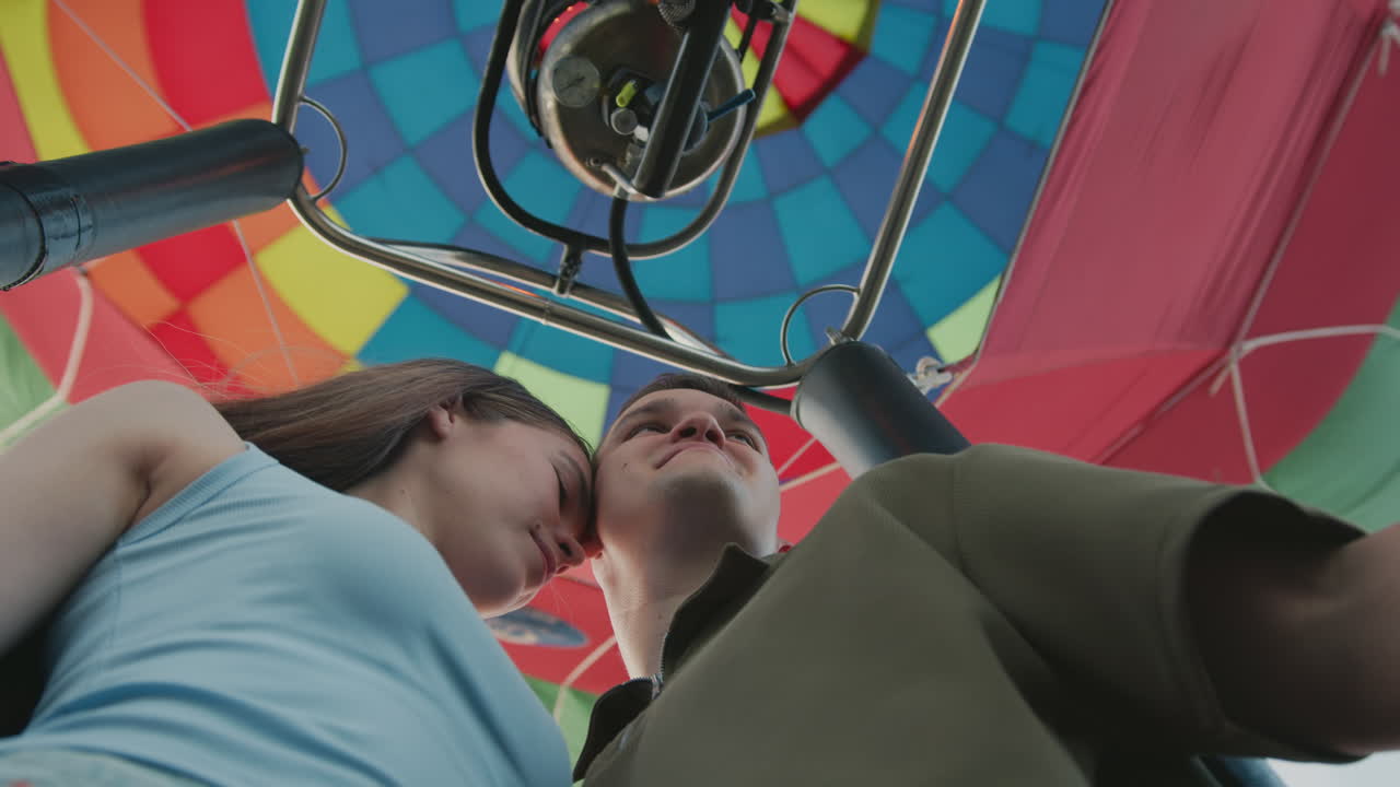 Low angle view of romantic couple enjoying special moment together inside vibrant hot air balloon, they gaze at each other warmly, surrounded by colorful panels