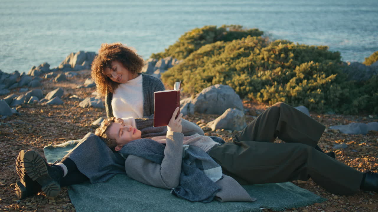 Happy sweethearts reading book ocean seashore cliff date. Man lying woman knees