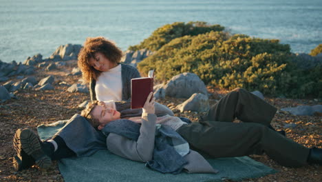 happy sweethearts reading book ocean seashore cliff date. man lying woman knees