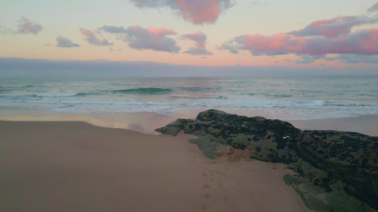 Foaming waves washing shore drone view. Sunset casting pastel glow over beach
