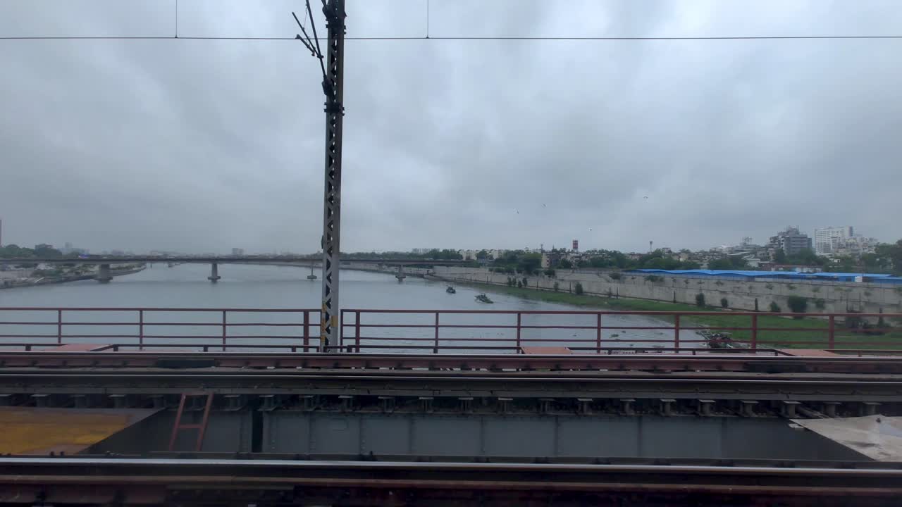 Sabarmati River view from moving train over bridge under cloudy monsoon weather