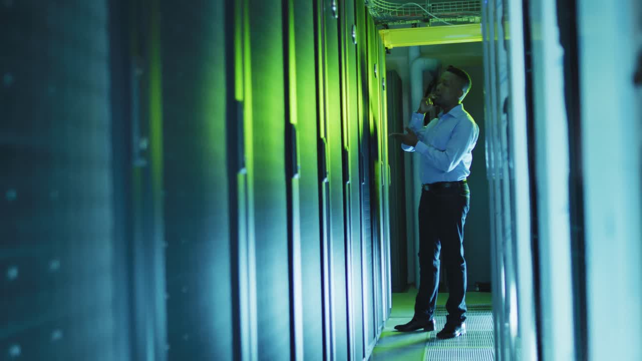 técnico informático afroamericano que usa un teléfono inteligente trabajando en una sala de servidores de negocios