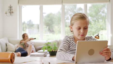 girl at table with digital tablet home schooling during health pandemic with family in background