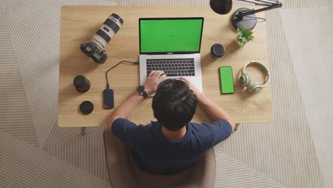 top view of a male video editor using green screen laptop and smartphone next to the camera in the workspace at home