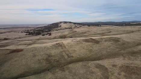 Drone-footage-over-scenic-hilly-grassland-and-trees-in-El-Dorado,-USA,-with-misty-mountains-in-the-distance