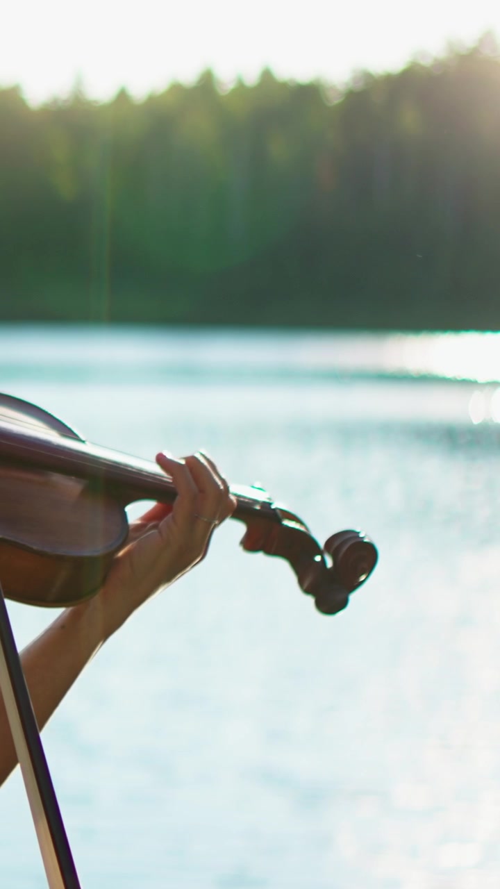 Musicista che suona il violino all'aperto vicino a un lago al tramonto.