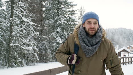 young handsome man with backpack walking in national park at snowy day and enjoying winter nature