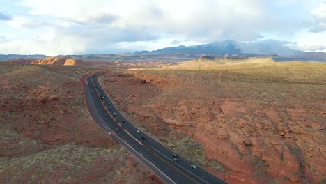 cars driving over a two lines wide black ashpalt interstate 15 road true the red canyon close to st george on a partly cloudy sunny day