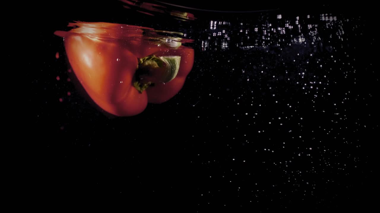 검은 배경에 거품이 있는 물에 떨어지는 고추 파프리카