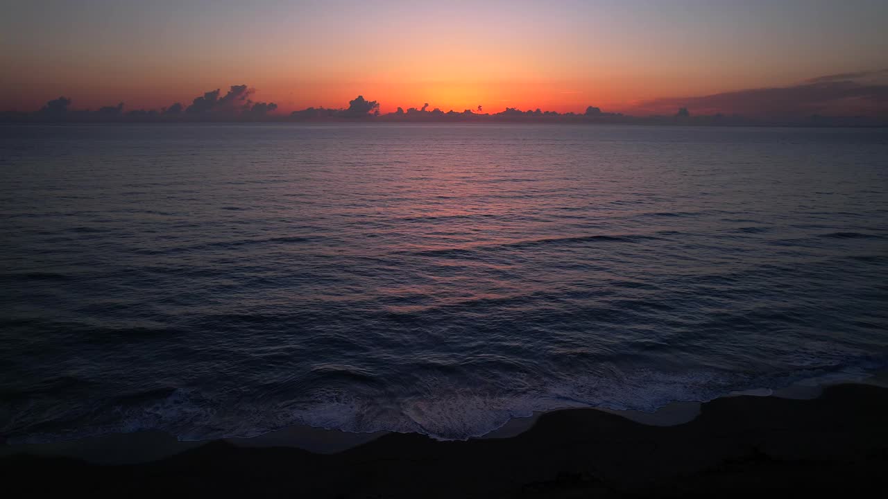 해변에서 해가 뜨는 동안 모래로 굴러가는 파도의 정적 공중 사진