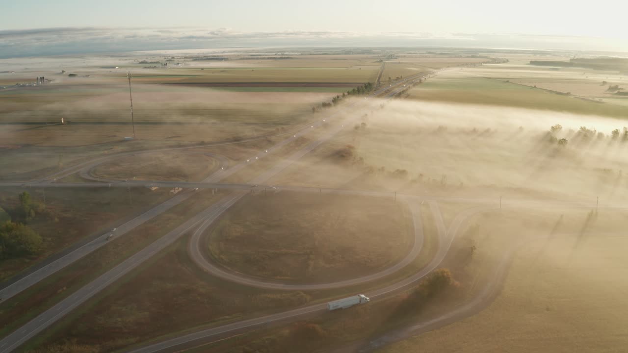Foggy morning over rural highway with traffic moving and truck parked on exit ramp. Dangerous driving in hazardous conditions. Weather and travel concept.