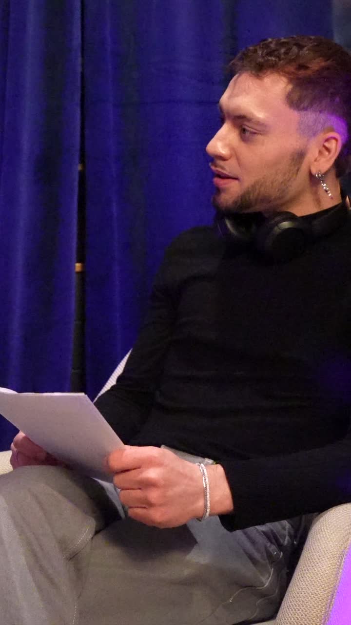 Young Man Sitting in Chair, Reading Papers and Smiling