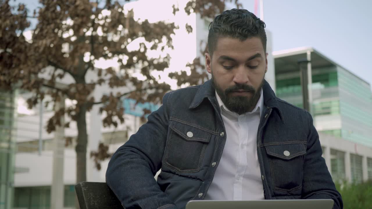 hombre enfocado escribiendo en una computadora portátil al aire libre