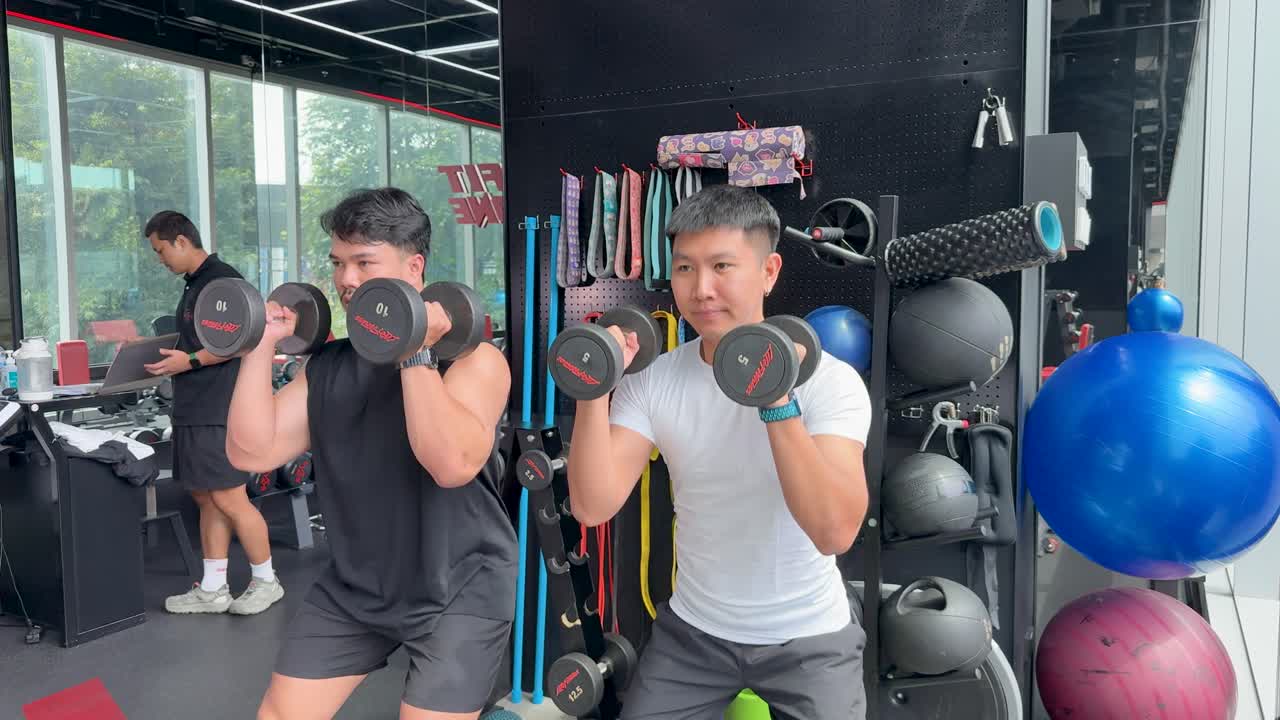 Two individuals perform a synchronized dumbbell workout in a well-equipped gym, showcasing strength and fitness