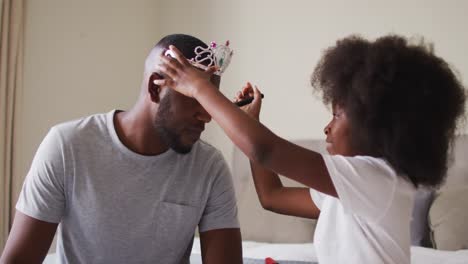 african american father wearing tiara having makeup put on by his daughter