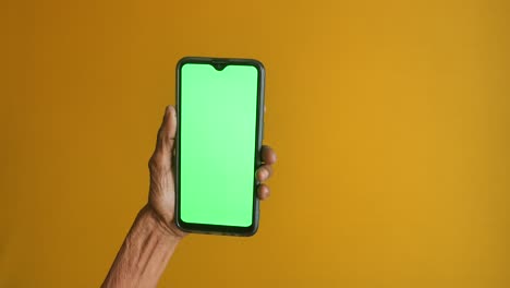 elderly hand holding smartphone with green screen