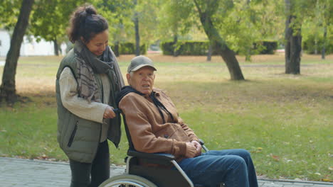 woman walking in park with grandfather in wheelchair