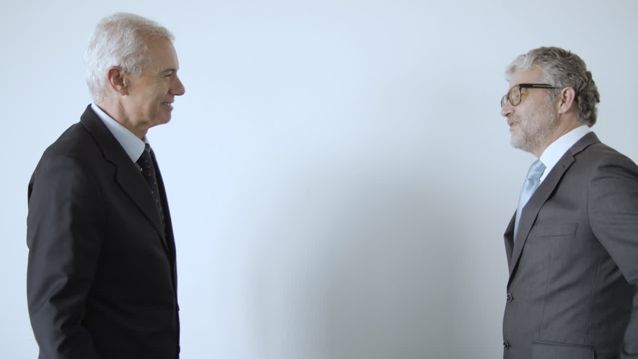 amables hombres de negocios maduros dándose la mano y de pie en la pared blanca