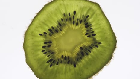 una rebanada de kiwi transparente giratoria sobre un fondo blanco.