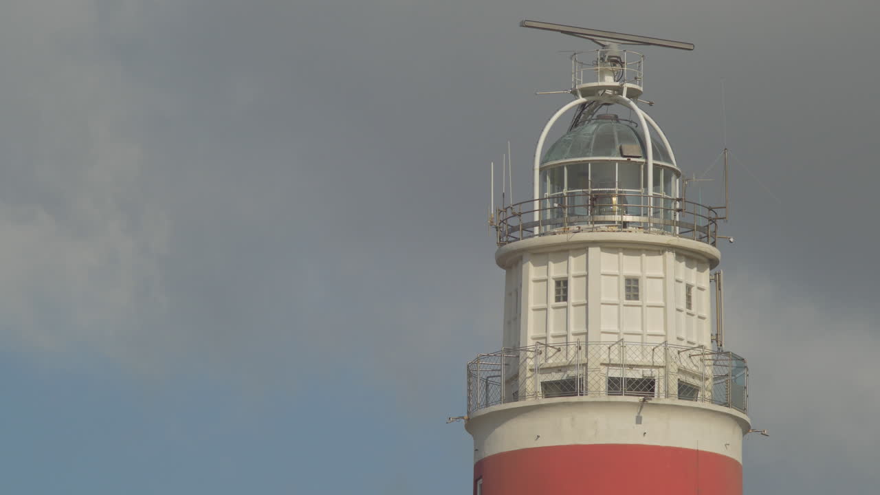 Close-up view of a red and white lighthouse against a cloudy sky
