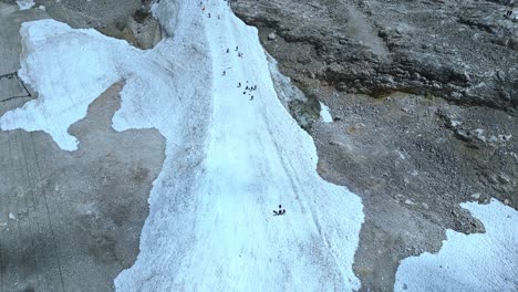 Aerial-view-of-winter-activities,-people-sledding-on-a-snow-covered-mountain,-next-to-a-contrast-of-dry-mountain-rocks