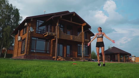 mujer delgada y hermosa en ropa deportiva en el fondo de la casa en el césped realiza saltos para el entrenamiento cardiovascular y la quema de grasa