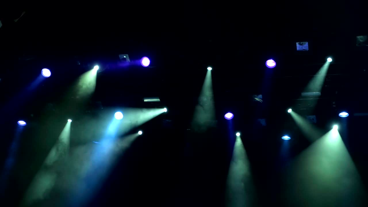 4k uhd handheld Lighting equipment on the stage of the concert during the performance. The light rays from the spotlight through the smoke. Blue and yellow  purple green rays of light