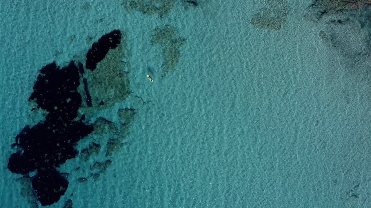 vista aérea desde un dron de un paddle boarder flotando sobre un arrecife poco profundo en la playa de son bou, españa