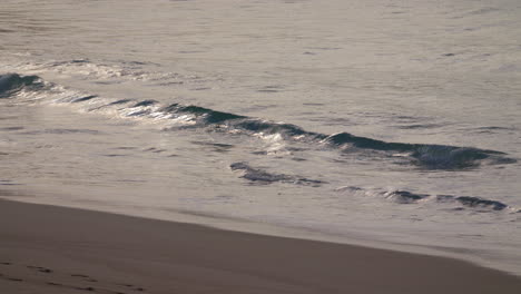 Manly-Beach-Sydney-Australia,-waves-crash-in-slow-motion-upon-the-sand-in-the-early-morning-with-the-sunrising-in-the-reflection