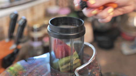 female hand placing pieces of fresh produce into juicer