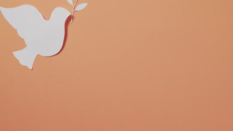 Close-up-of-white-dove-with-leaf-and-copy-space-on-orange-background