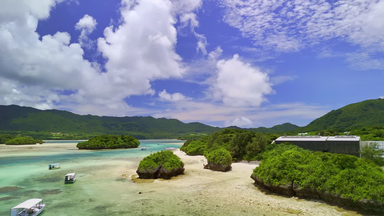 Aerial drone footage pans over the stunning turquoise waters and green islets of Kabira Bay, Ishigaki, Okinawa, Japan. A beautiful, sunny day in a tropical paradise with tour boats below