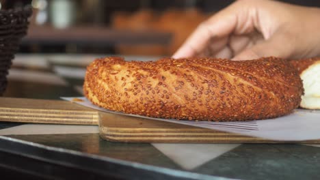 a hand breaking a traditional turkish simit (bagel) with sesame seeds