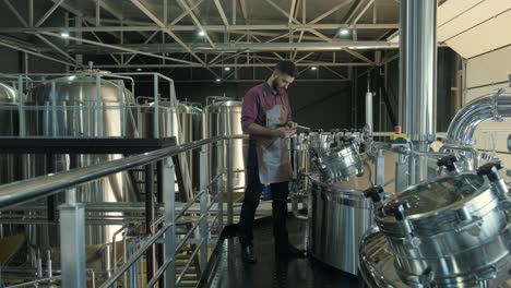 un joven cervecero con un delantal de cuero supervisa el proceso de fermentación de la cerveza en una fábrica de cerveza moderna