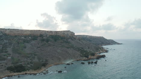 Wide-View-of-Coastline-of-Gozo,-Malta-Island-at-Sunset-with-Cliff-and-Ocean-Waves,-Aerial-reverse-dolly-backwards