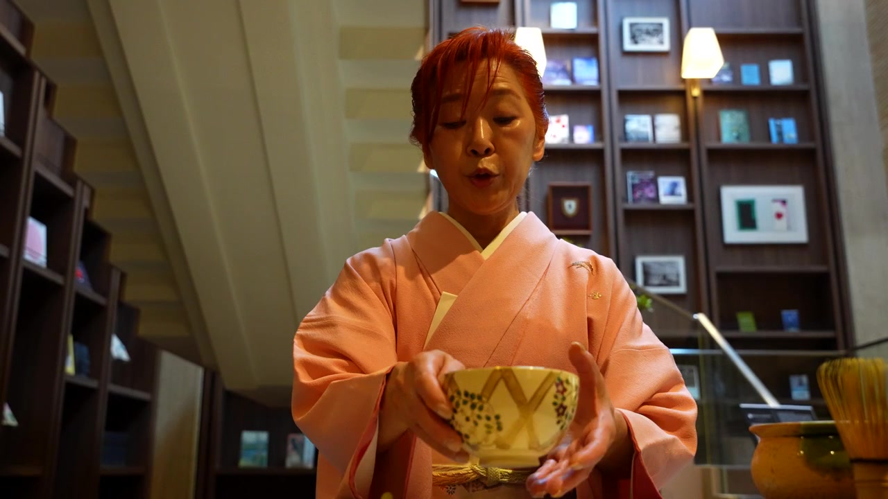 Woman in traditional pink kimono performing a Japanese tea ceremony, preparing matcha with a bowl