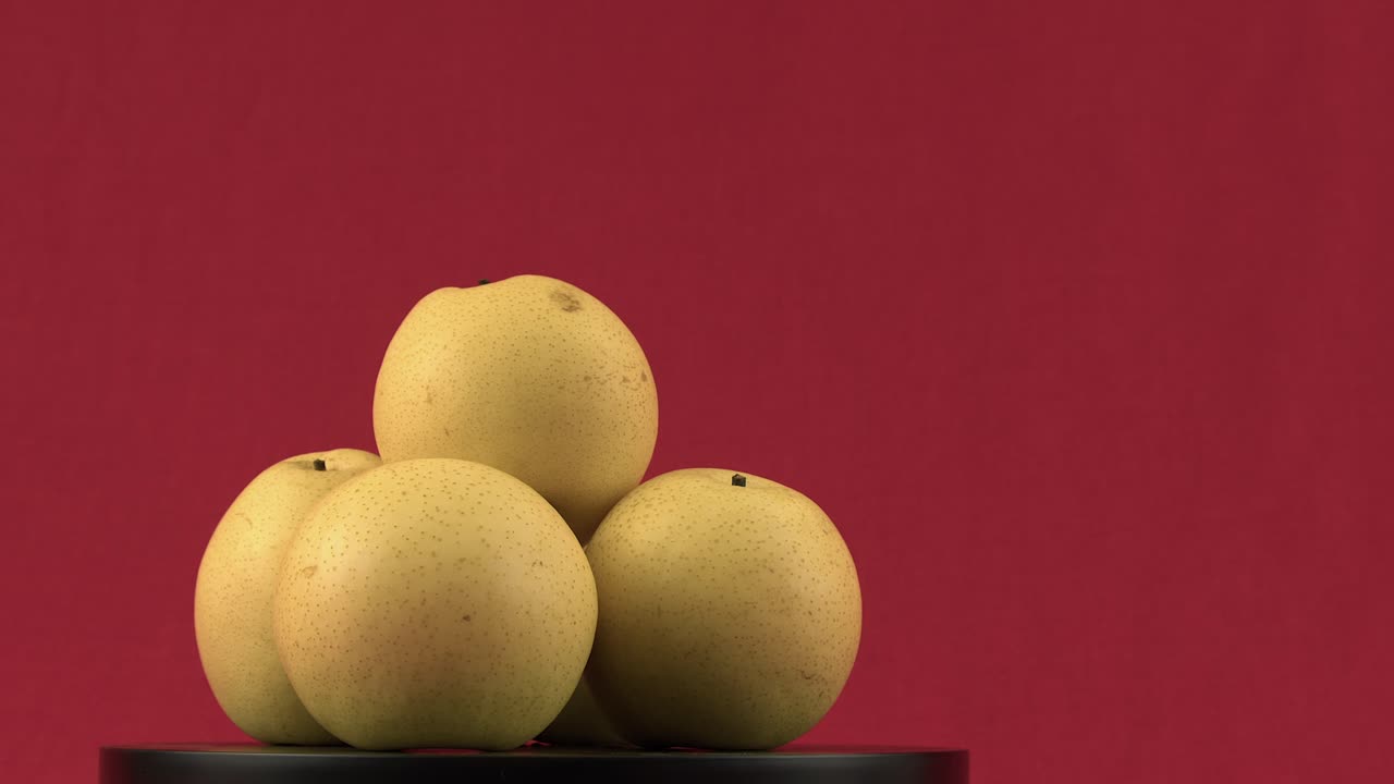 Pila di pere mela gialle che ruotano su un piatto girevole su sfondo rosso.