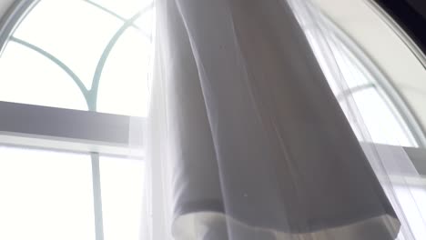 Slow-pan-downwards-of-a-beautiful-wedding-dress-hanging-from-large-window-sill