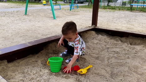 cute baby boy playing with his toy in the sandbox. kid splashing water in the bucket with his hand.