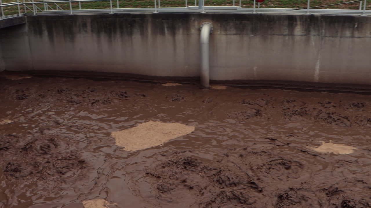 Una vasca di acque reflue color cioccolato si agita e ribolle nell'impianto di trattamento mentre la telecamera esegue una panoramica fluida da destra a sinistra, rivelando il processo industriale in corso.