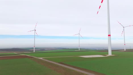 Spinning-Giant-Wind-Turbines-Over-Verdant-Nature-At-Sunrise