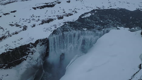 Dettifoss-Waterfall,-Iceland-in-Winter-Season,-Cold-Glacial-Water-and-Snow-Capped-Volcanic-Cliffs,-Drone-Shot