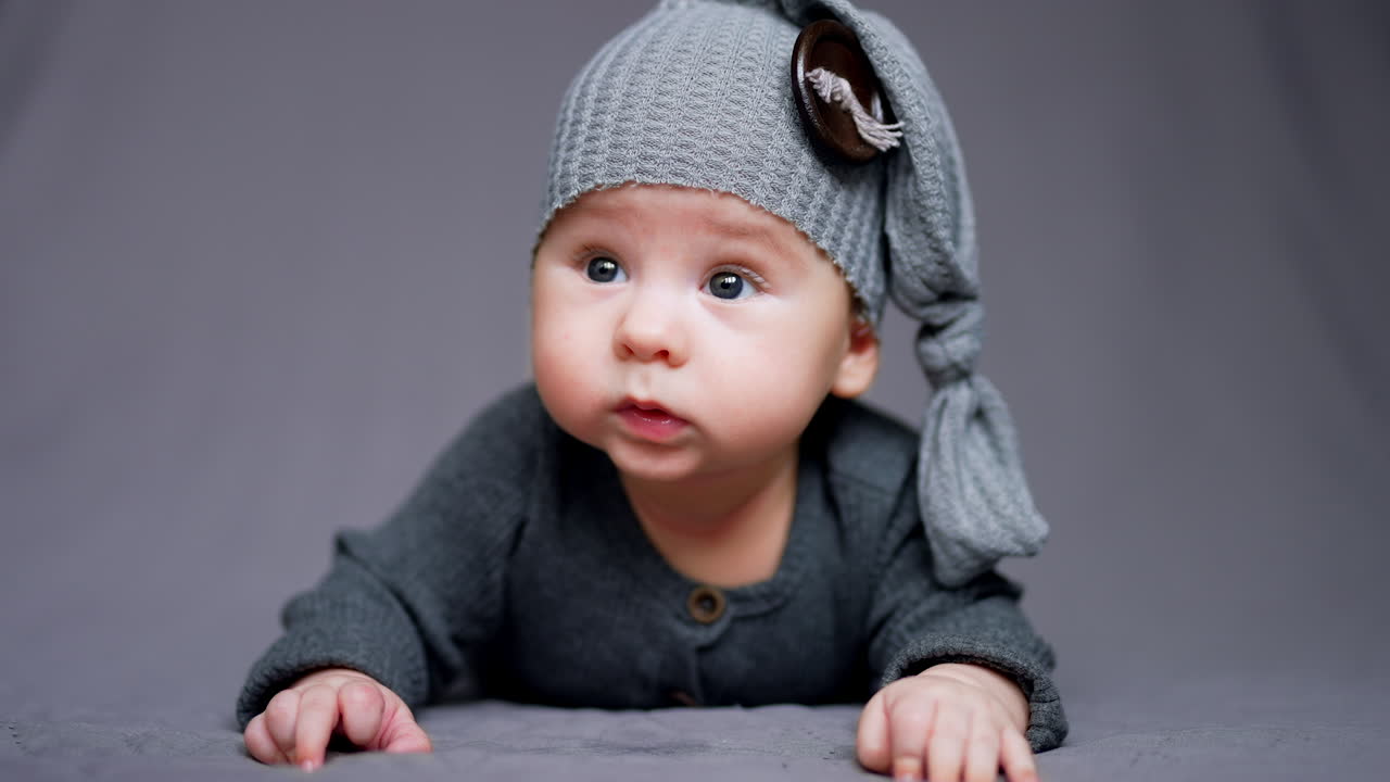 Small kid in grey clothes and hat with huge button. Close up portrait of a child in funny cap. Blurred grey backdrop.