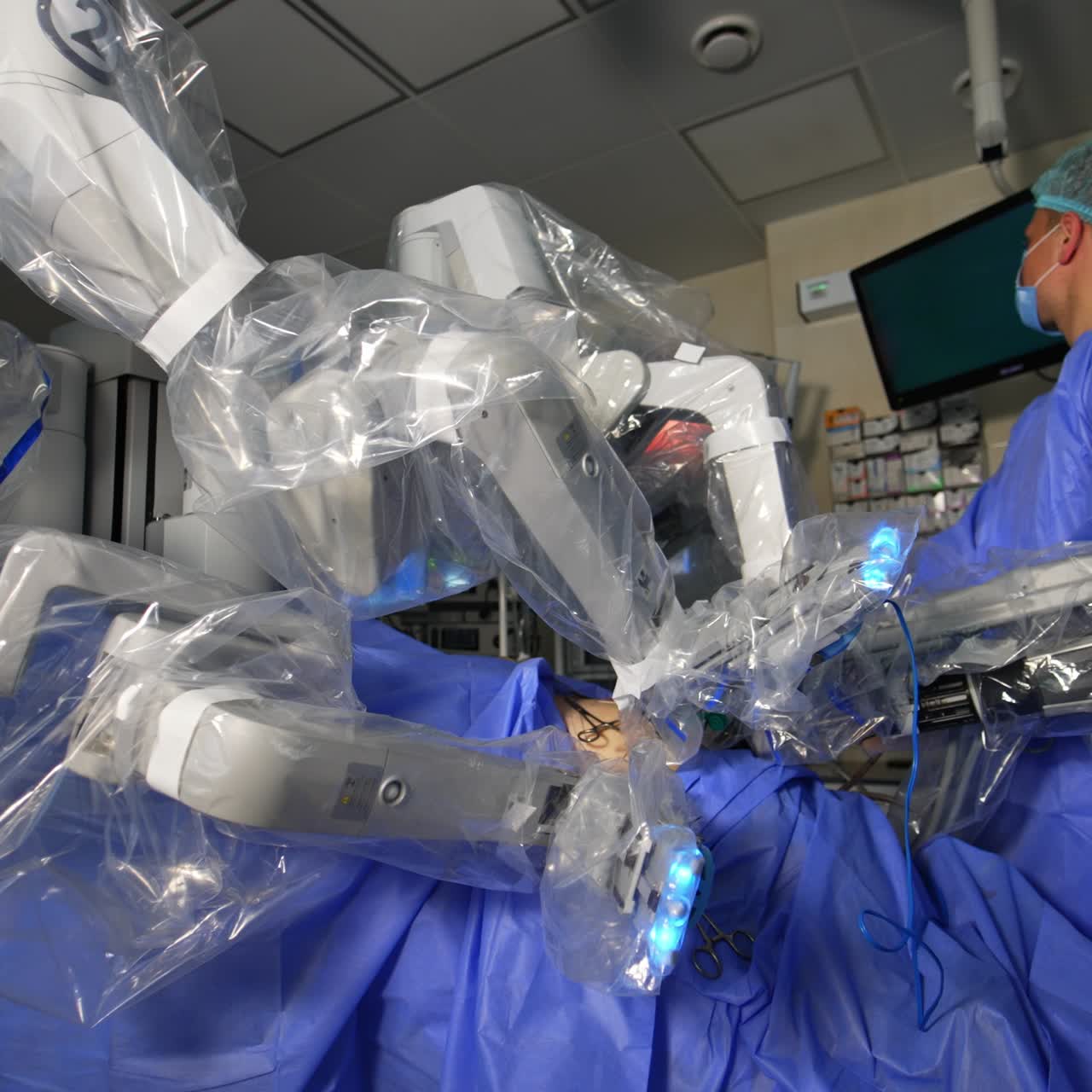 Robotic surgeon covered with plastic for sterility in surgery room. Male doctor stands in the operative field and looks attentively on the screen
