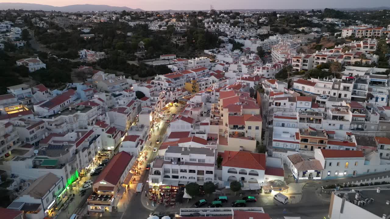 al atardecer una gran altitud hecho vuela horizontalmente de derecha a izquierda sobre carvoeiro portugal algarve con coches gente tiendas y restaurantes en verano