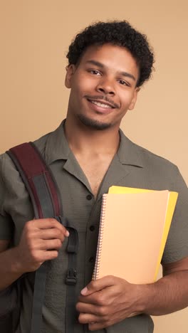 happy male university student with backpack and books in beige studio