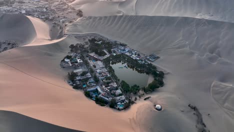 Oasis-Del-Desierto-Huacachina,-Perú-Con-Lago-Y-Palmeras,-Con-Grandes-Dunas-De-Arena-En-El-Fondo