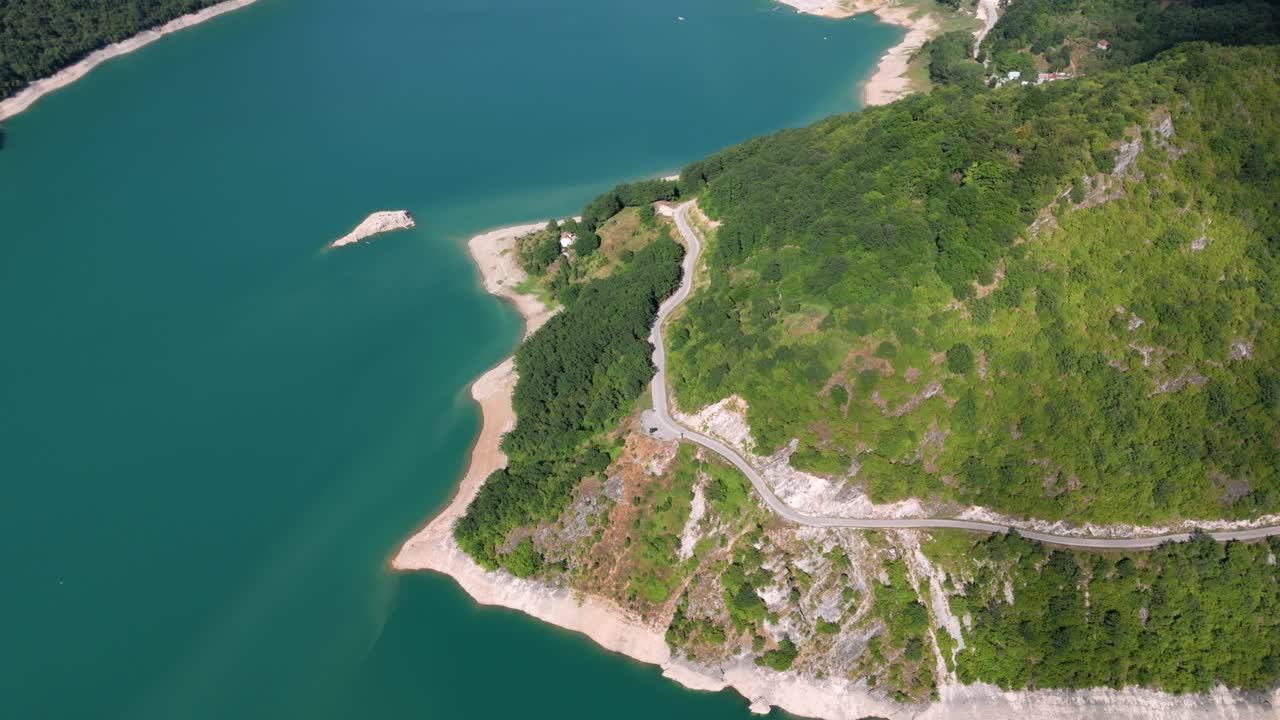 Flying over the turquiose lake Pivsko near Pluzine in the distance surrounded by green forrests and mountains in Montenegro during august summertime showing the beutiful wide landscape